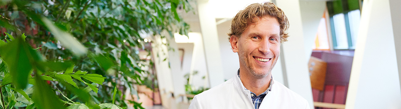 Medisch specialist Matthias staand in ziekenhuishal bij plantenbak